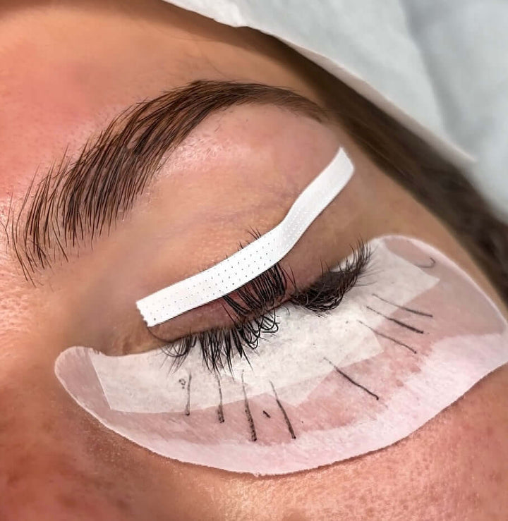 Eyelash extension application with slim white lash tape to secure lower lashes and protective pad