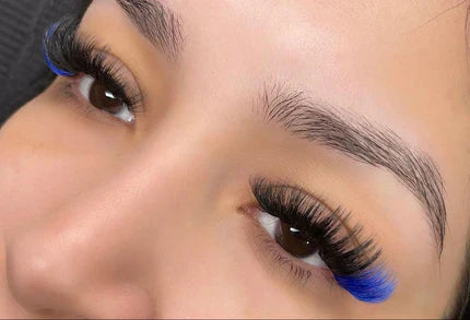 A person has long, thick eyelashes with blue tips, complemented by well-groomed eyebrows.