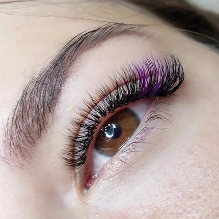 A close-up of an eye with dramatic eyelash extensions, featuring a mix of black and purple lashes.