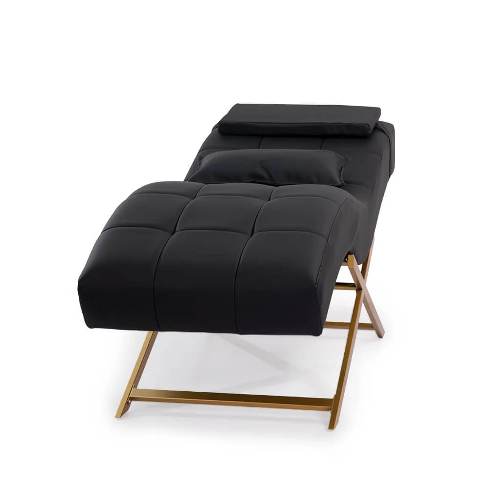 A black leather chaise lounge with a gold X-shaped base is angled on a white background.