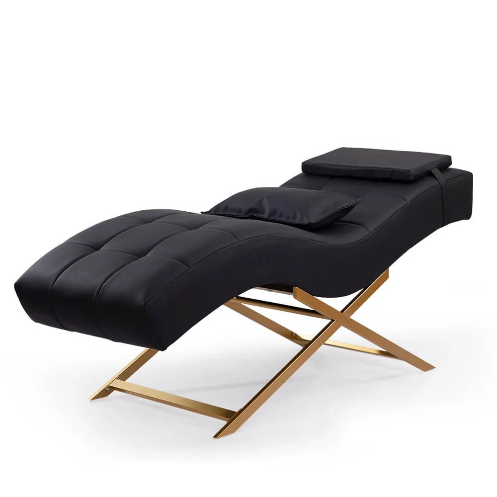 A sleek black leather chaise lounge with a golden X-shaped base is presented against a white background.
