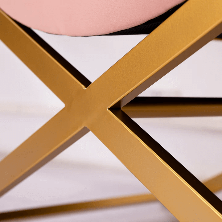 A close-up photo of the crisscross gold metal legs of a pink velvet chaise lounge.