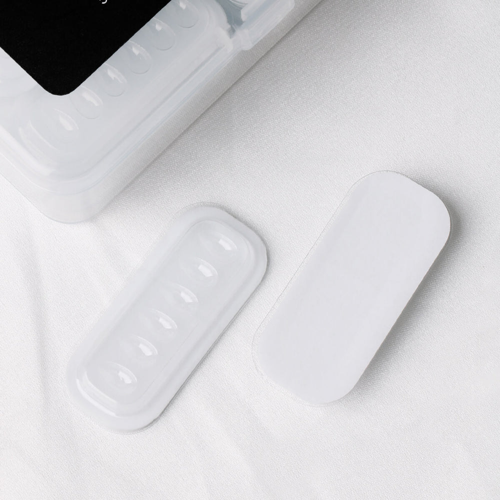 A clear plastic tray with six wells and a white adhesive strip on a white fabric background.