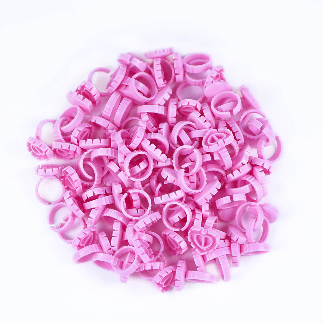 A pile of pink Sweet Heart Glue Cups for eyelash extensions, scattered on a white background.