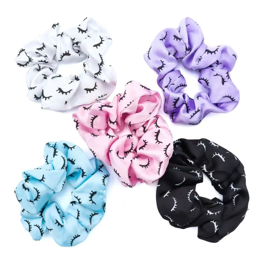 Satin lash scrunchies in various colors: white, purple, pink, blue, and black, with eyelash pattern. 